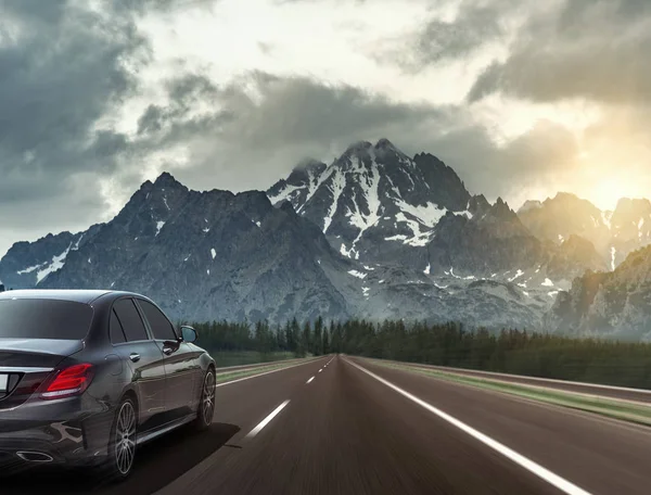 El coche conduce rápido en la carretera contra el telón de fondo de una cordillera . — Foto de Stock