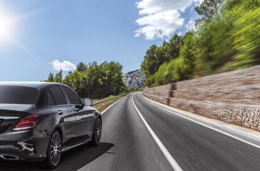 Araba, güneşli bir yaz gününde bir dağ yolunda hareket eder..