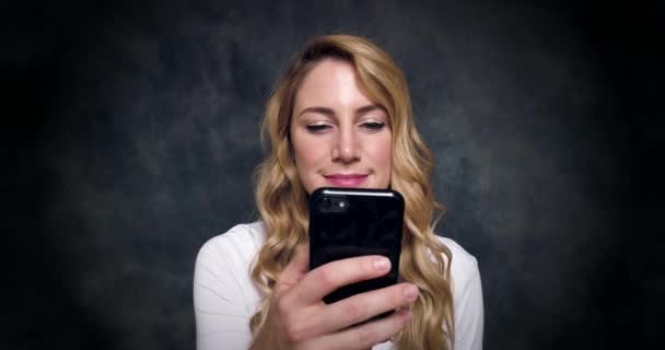 Atraktivní blondýnka hovoří mobilním telefonem na tmavém pozadí.. — Stock video