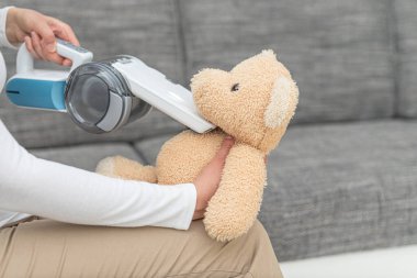 Elinde taşınabilir elektrikli süpürgeyle oyuncak ayıyı vakumlayan bir kadın..