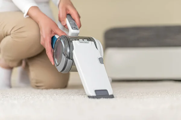 Mujer aspirando muebles en una casa con una aspiradora portátil de mano . — Foto de Stock