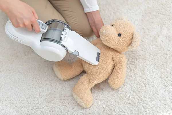 Mujer aspirando osito de peluche en una casa con una aspiradora portátil de mano . — Foto de Stock