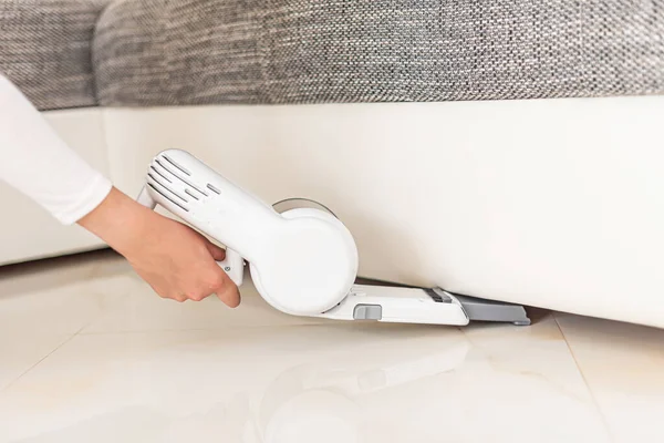 Mujer aspirando muebles en una casa con una aspiradora portátil de mano . — Foto de Stock