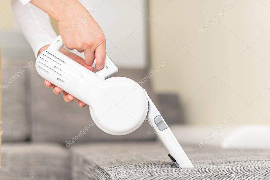 Woman vacuuming furniture in a house with a hand-held portable vacuum cleaner.