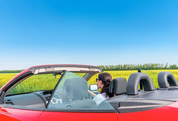Kırmızı arabalı bir kadın şehir dışındaki bir tarlanın arka planında.. — Stok fotoğraf