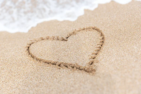 Καρδιά σύμβολο γραμμένο σε μια αμμώδη παραλία με αφρό και νερό φόντο. — Φωτογραφία Αρχείου