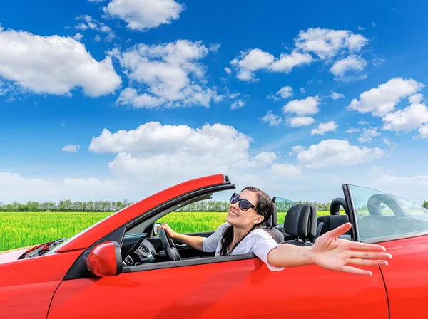 Mujer en un coche rojo en el fondo de un campo fuera de la ciudad . — Foto de Stock