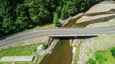 Dağlardaki ormanın arka planında nehrin üzerindeki otomobil köprüsü..