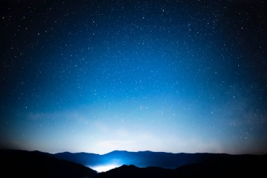 Yıldızlı gece gökyüzü dağların üzerinde panorama şehir ışıkları altında