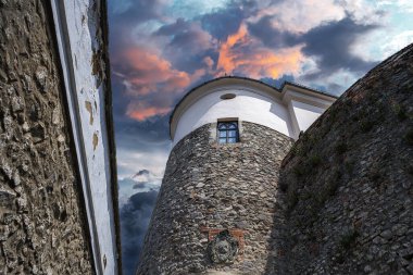 Kadim taş kale kulesi ve onun güçlendirilmiş duvarları renkli günbatımı bulutlarıyla dolu canlı bir gökyüzüne karşı..