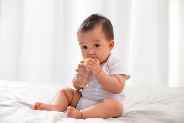 可爱的亚洲婴儿坐在床上 喝婴儿奶瓶的水的全长视图 — 图库照片
