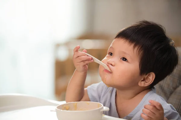 Adorable Asiático Niño Comiendo Con Cuchara Mirando Arriba Casa —  Fotos de Stock