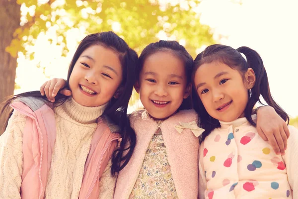 秋の公園で抱きしめている3人の愛らしい笑顔のアジアの子供たちの低角度の眺めとカメラを見て — ストック写真