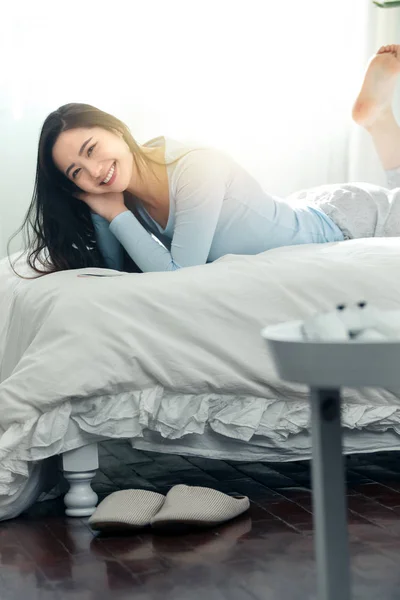 美丽的快乐年轻的亚洲女人在睡衣躺在床上 微笑着对着相机 — 图库照片