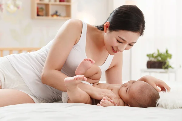 ベッドに横たわって愛らしい赤ちゃんと遊んで微笑む若い母親 — ストック写真