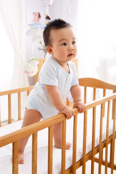 The baby is standing on the little bed. — Stock Photo, Image