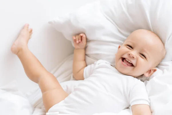 Chłopiec Leżący Białym Łóżku Śmiejący Się Szczęśliwie — Zdjęcie stockowe