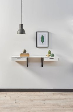 Beyaz asılmış masa beyaz duvar çerçeve lamba ve vazo bitki.