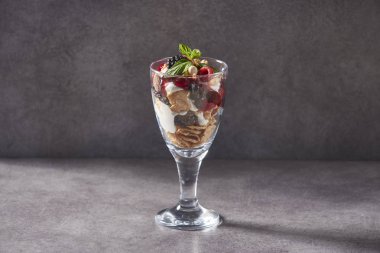 servis tarzı için cam üzerinde müsli, yoğurt, taze ahududu, yaban mersini ve sağlıklı kahvaltı gri arka plan için fındık ile yulaf granola kase