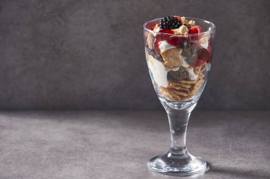 servis tarzı için cam üzerinde müsli, yoğurt, taze ahududu, yaban mersini ve sağlıklı kahvaltı gri arka plan için fındık ile yulaf granola kase