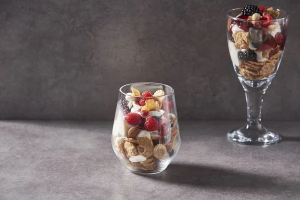 muesli on the glasses for service style, bowl of oat granola with yogurt, fresh raspberries, blueberries and nuts for healthy breakfast grey background