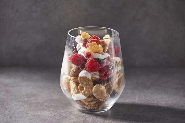 muesli on the glass for service style, bowl of oat granola with yogurt, fresh raspberries, blueberries and nuts for healthy breakfast grey background