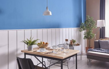 Modern yemek odası dekorasyon, ahşap masa ve siyah sandalye. Mavi ve beyaz duvar arka plan. Klasik duvar detay. Gri mobilya, orta masa, kanepe ve mavi koltuk. Hasır halı ve beyaz lamba.