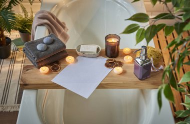 Modern banyo oda ve spa merkezi beyaz küvet ahşap masa. Mumlar, havlu ve sabun tarzı bitkiler ile. Beyaz mermer zemin duvar