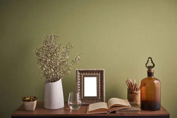 Decorative desk and table style and vase of plant frame glass of water and book on the desk interior room with green wall background