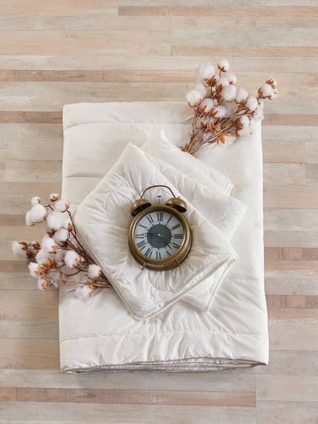 White quilt and pillow style with cotton on the parquet, clock object.