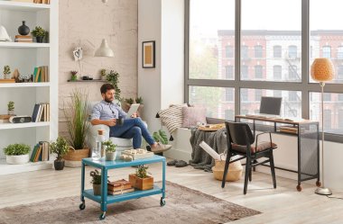 Odada bir adam var, köşe başı tarzı, dizüstü bilgisayarla müzik dinliyor ve evden çalışıyor. Modern dekorasyon biçimi.