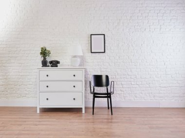 Tuğla duvar, lamba, çerçeve ve vazo önünde dekoratif beyaz dolap ve siyah sandalye.