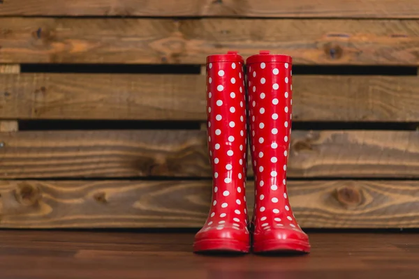 Ahşap arka plan üzerinde beyaz polka noktalı kırmızı lastik çizmeler