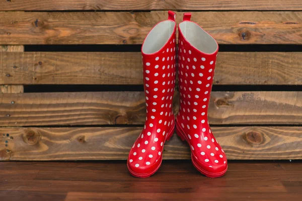 Ahşap arka plan üzerinde beyaz polka noktalı kırmızı lastik çizmeler