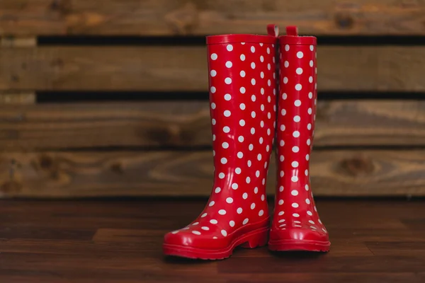 Ahşap arka plan üzerinde beyaz polka noktalı kırmızı lastik çizmeler