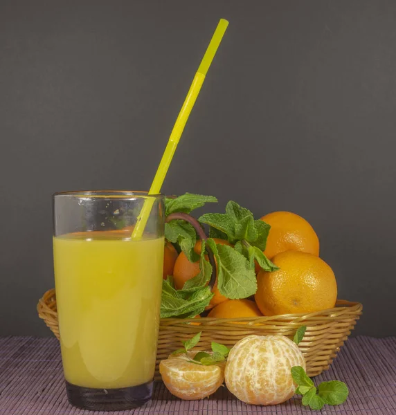 A basket of tangerines with mint and a glass of juice from them. — Stock Photo, Image