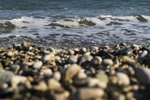 Tengeri hullám a kavicsos tengerparton, előtér a fókuszon kívül. — Stock Fotó