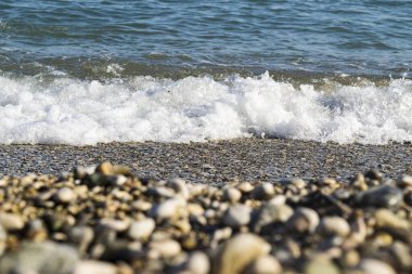 Çakıl taşlı sahilde deniz dalgaları, odak dışı ön plan.