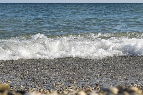 Onda marina su una spiaggia di ciottoli, primo piano fuori fuoco . — Foto Stock