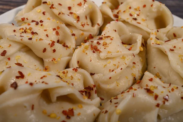 Boiled manti with beef on a plate with spices on a wooden table. Close up. — Stock Photo, Image