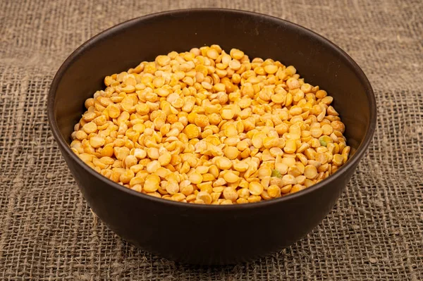 Yellow split peas in a ceramic bowl on a background of coarse-textured burlap. Traditional cereals for making soups and porridge. Close up