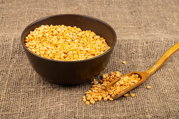 Yellow split peas in a ceramic bowl on a background of coarse-textured burlap. Traditional cereals for making soups and porridge. Close up — Stock Image Yellow Split Peas Ceramic Bowl Background Coarse Textured Burlap Traditional Stock Photo