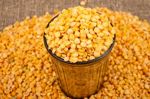 Yellow split peas in a cut glass and grits scattered on a background of coarse-textured burlap. Traditional cereals for making soups and porridge. Close up — Stock Image Yellow Split Peas Cut Glass Grits Scattered Background Coarse Textured Royalty Free Stock Images