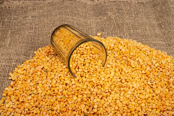 Yellow split peas in a cut glass and grits scattered on a background of coarse-textured burlap. Traditional cereals for making soups and porridge. Close up