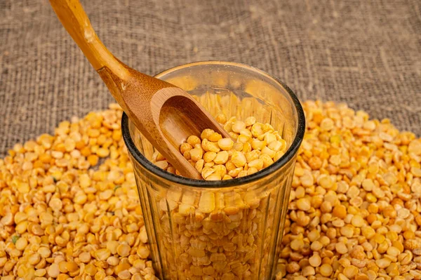 Yellow split peas in a cut glass and grits scattered on a background of coarse-textured burlap. Traditional cereals for making soups and porridge. Close up — Stock Image Yellow Split Peas Cut Glass Grits Scattered Background Coarse Textured Stock Image