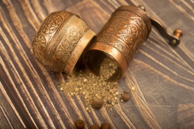Açık bir manuel baharat değirmeni ve ahşap bir masaya serpiştirilmiş tüm baharatlar. Kapat.