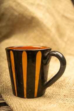 Kabataslak desenli ev yapımı kumaşın arka planında seramik kahve kupası. Kapat.