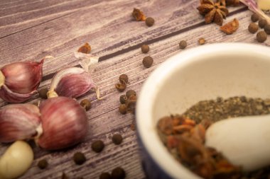 Seramik bir havanda baharat ve dağınık sarımsak karanfilleri, yıldız anason ve ahşap bir masanın üzerindeki tüm baharatlar. Kapat.