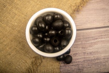 Seramik bir kasede çekirdeksiz zeytinler ve kabarık desenli kumaştan bir arka planda dağınık zeytinler. Kapat.