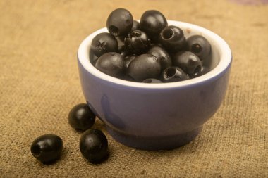 Seramik bir kasede çekirdeksiz zeytinler ve kabarık desenli kumaştan bir arka planda dağınık zeytinler. Kapat.